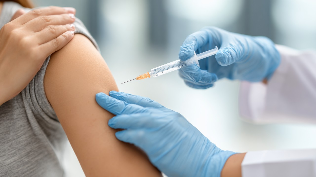 Close-up of healthcare professional administering a vaccine injection to a person's arm in a clinical setting, emphasizing immunization before travel.
