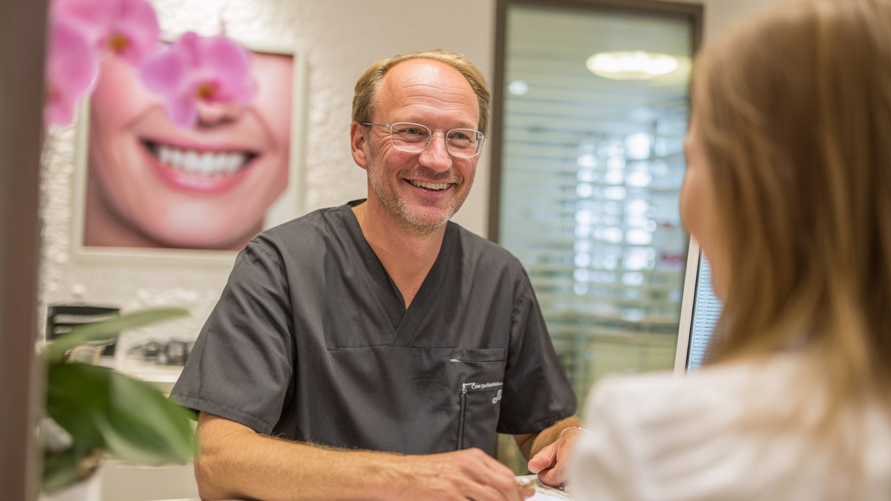 German plastic surgeon consulting with patient during follow-up in a clean, welcoming clinic, demonstrating attentive care and recovery support.