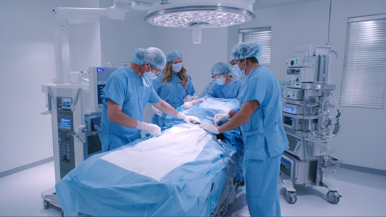 Medical surgeon performing body contouring and fat transfer procedure in a modern, well-lit surgical clinic with medical staff in scrubs.