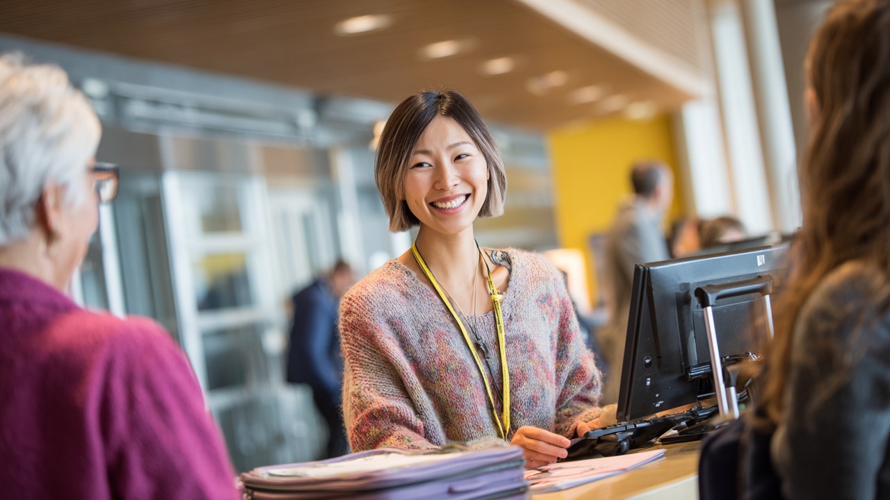 Multilingual patient coordinator assisting international cardiac care visitor and family at hospital reception with travel documents and luggage in a modern, patient-centered hospital.