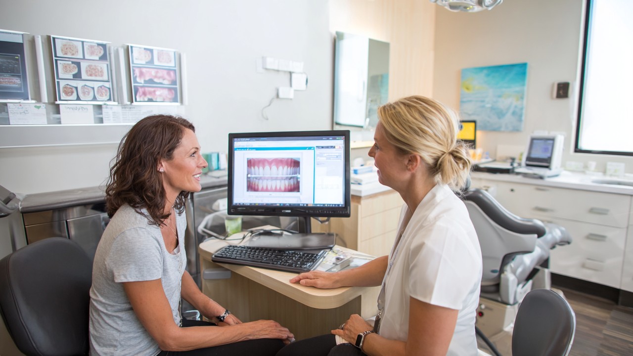 Paciente consultando com dentista em clínica, com escaneamentos 3D dentais e gráficos médicos para planejamento de implantes dentais.