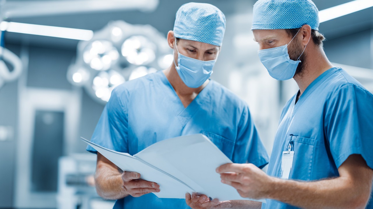 Close-up of a dental surgeon and orthopedic specialist reviewing patient charts in a sterile, modern operating room with advanced medical technology.