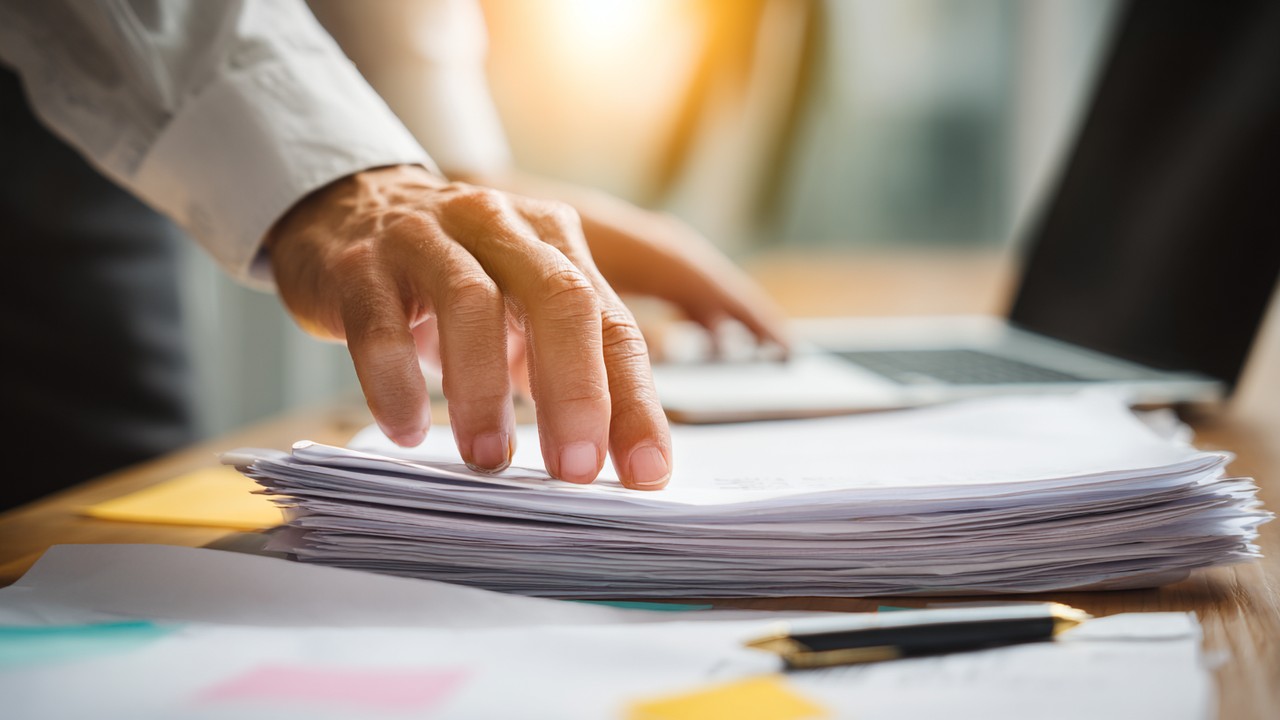 Close-up of hands organizing medical reports, passport, and visa application forms on a desk with a laptop and pen for medical visa preparation.