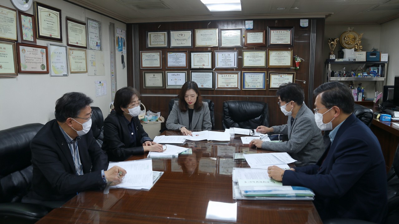 韩国医疗监管官员在会议室审查诊所认证文件,墙上悬挂证书和专业奖项,彰显严格监管与高标准。