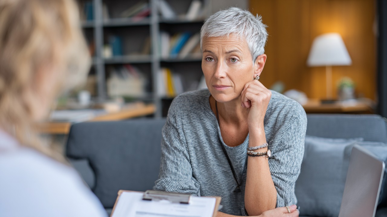 Middle-aged patient and healthcare consultant discussing treatment options in a comfortable consultation room, reviewing documents and laptop.